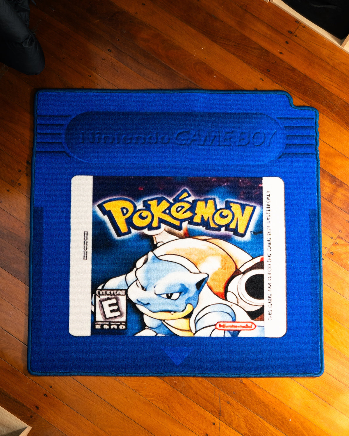 Pokemon Blue cartridge cut-out rug laid out on a floor
